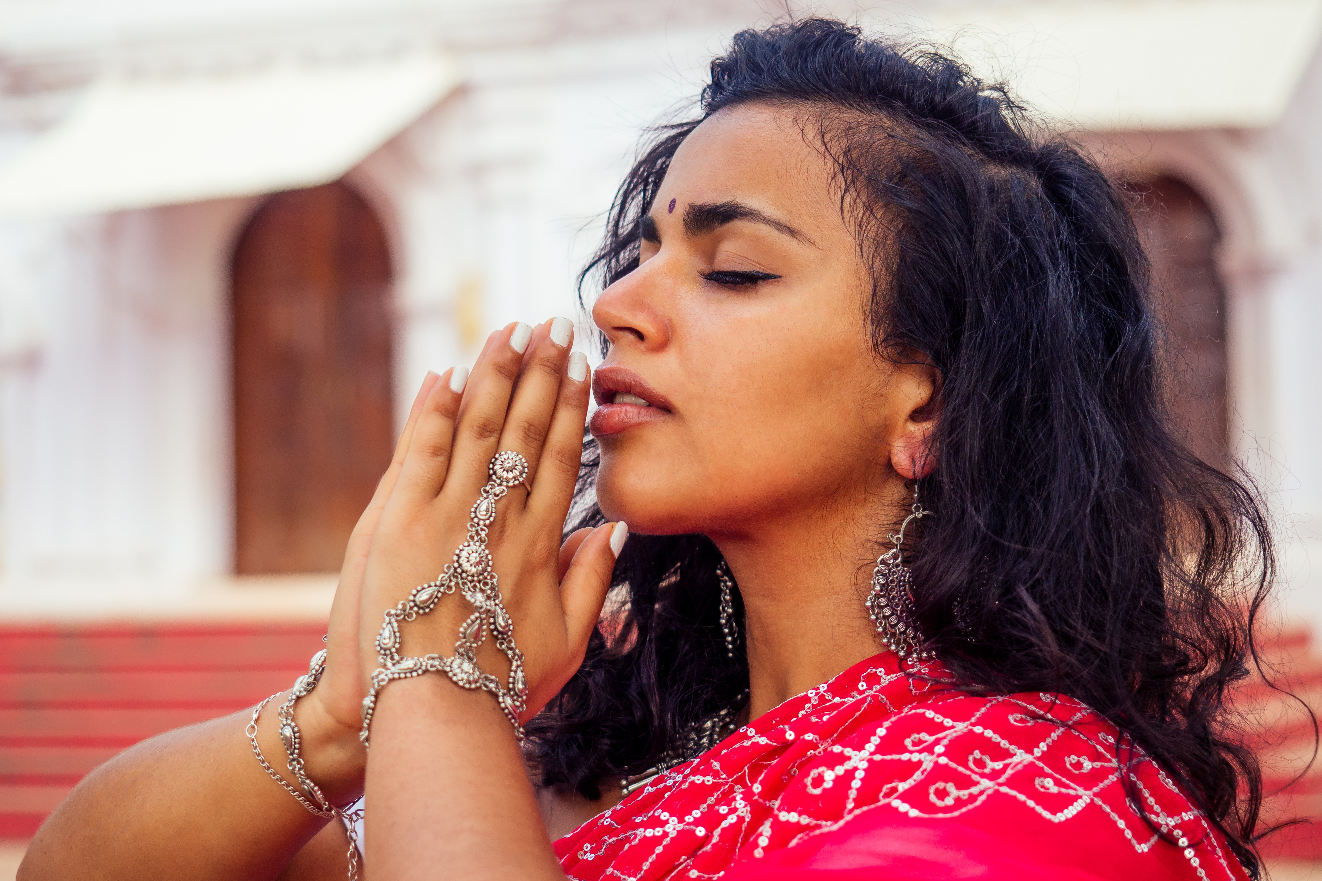 Young Indian woman in traditional sari red dress praying in a hindu temple goa